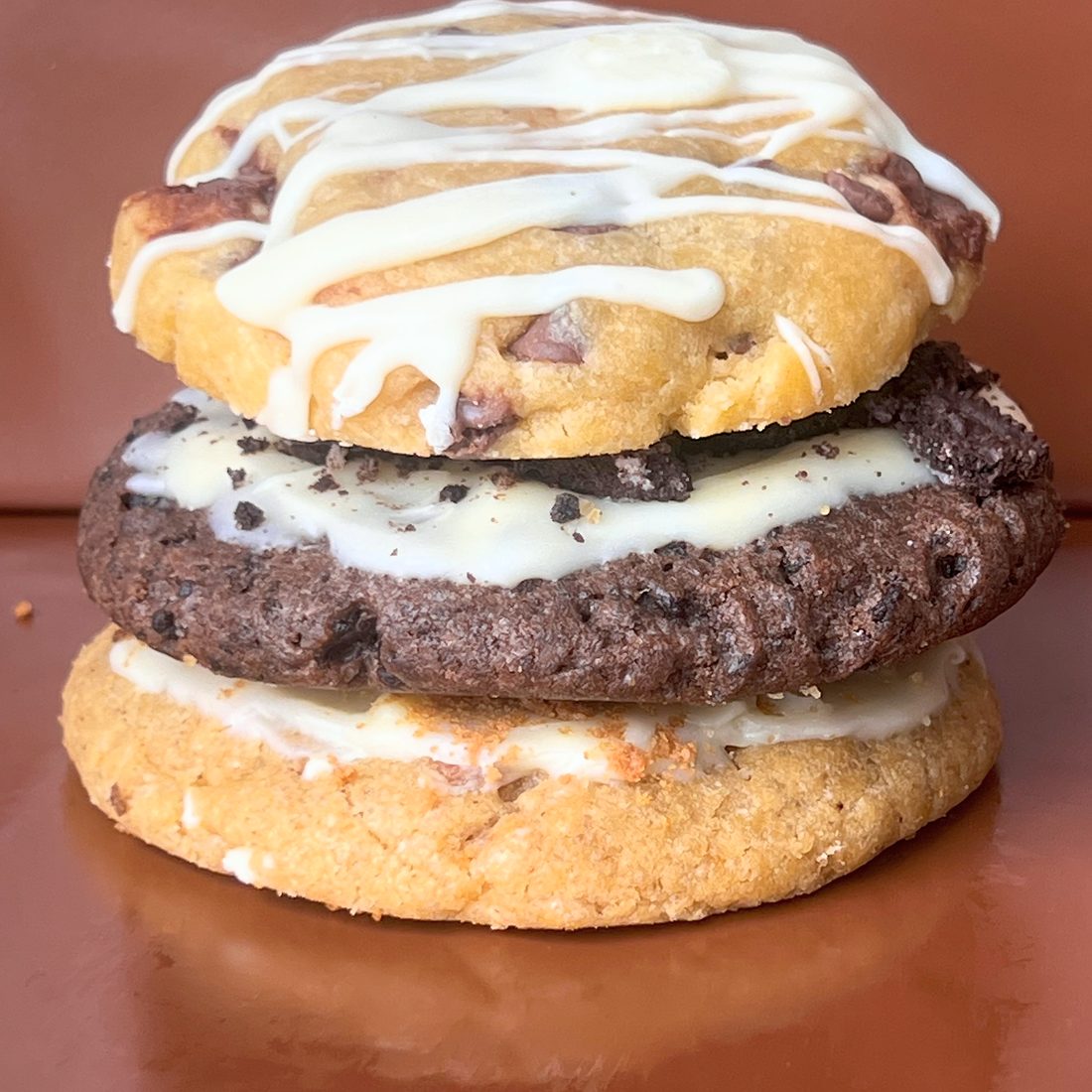 A stack of three MELT. cookies: Hazelnut Choc Chip on top, Oreo & Cream in the middle and Biscoff & Cream at the bottom